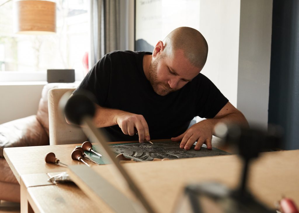 Artist Andrew Campe sitting at a table creating a linoprint